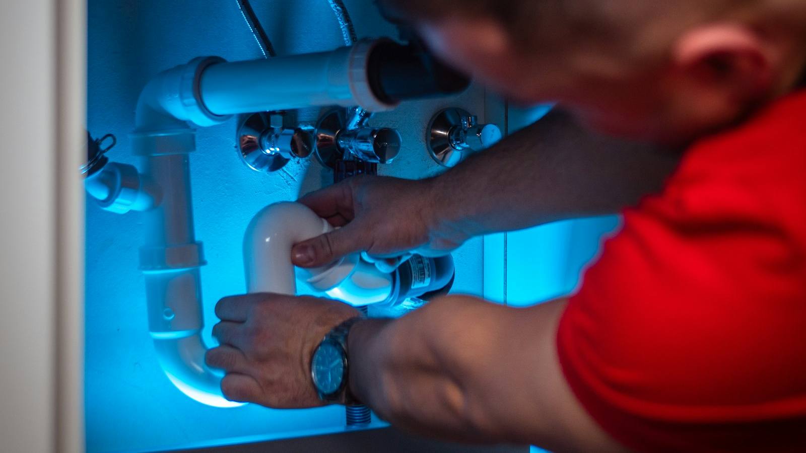 Technicien en intervention sous un meuble, les mains sur une canalisation